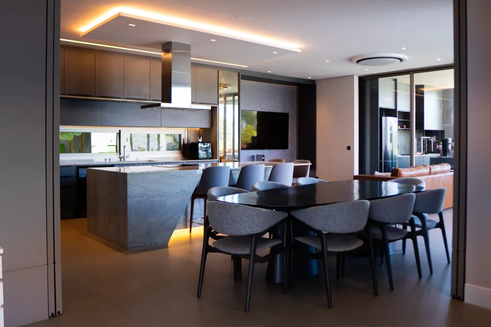 Cozinha contemporânea integrada à sala de jantar, com ilha em pedra e iluminação indireta